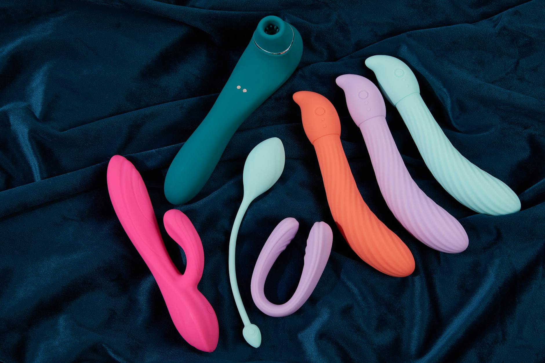 A vibrant orange vibrator held in hand against a minimalistic purple backdrop