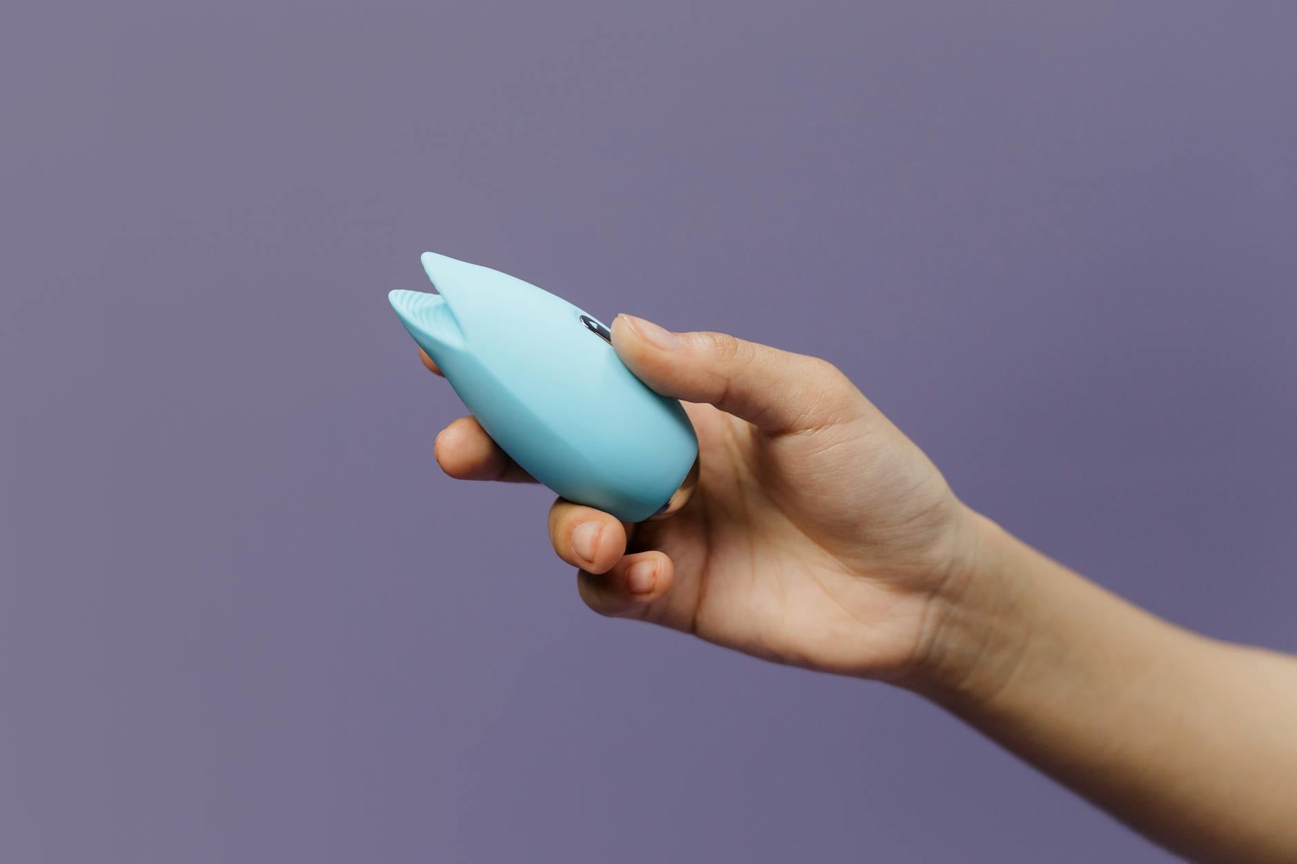 Intimate close-up of hands holding a sleek lemon-colored vibrator against a purple background